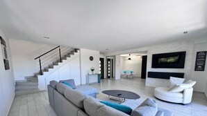 A modern living room with a grey sectional sofa, a round coffee table, and a white armchair. A staircase with a black railing leads to another level.