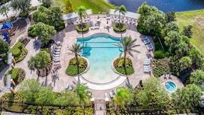 An aerial view of a resort with a central swimming pool, surrounded by lounge areas and palm trees. - Serenity Now by Shine Villas at Watersong #416 (Davenport)