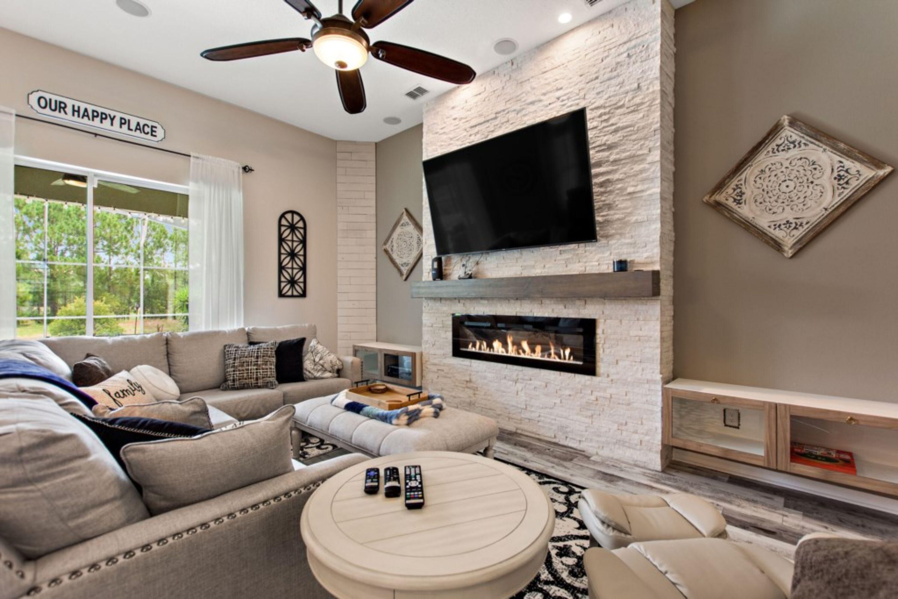 A modern living room with a fireplace, a large flat-screen TV, and a ceiling fan.