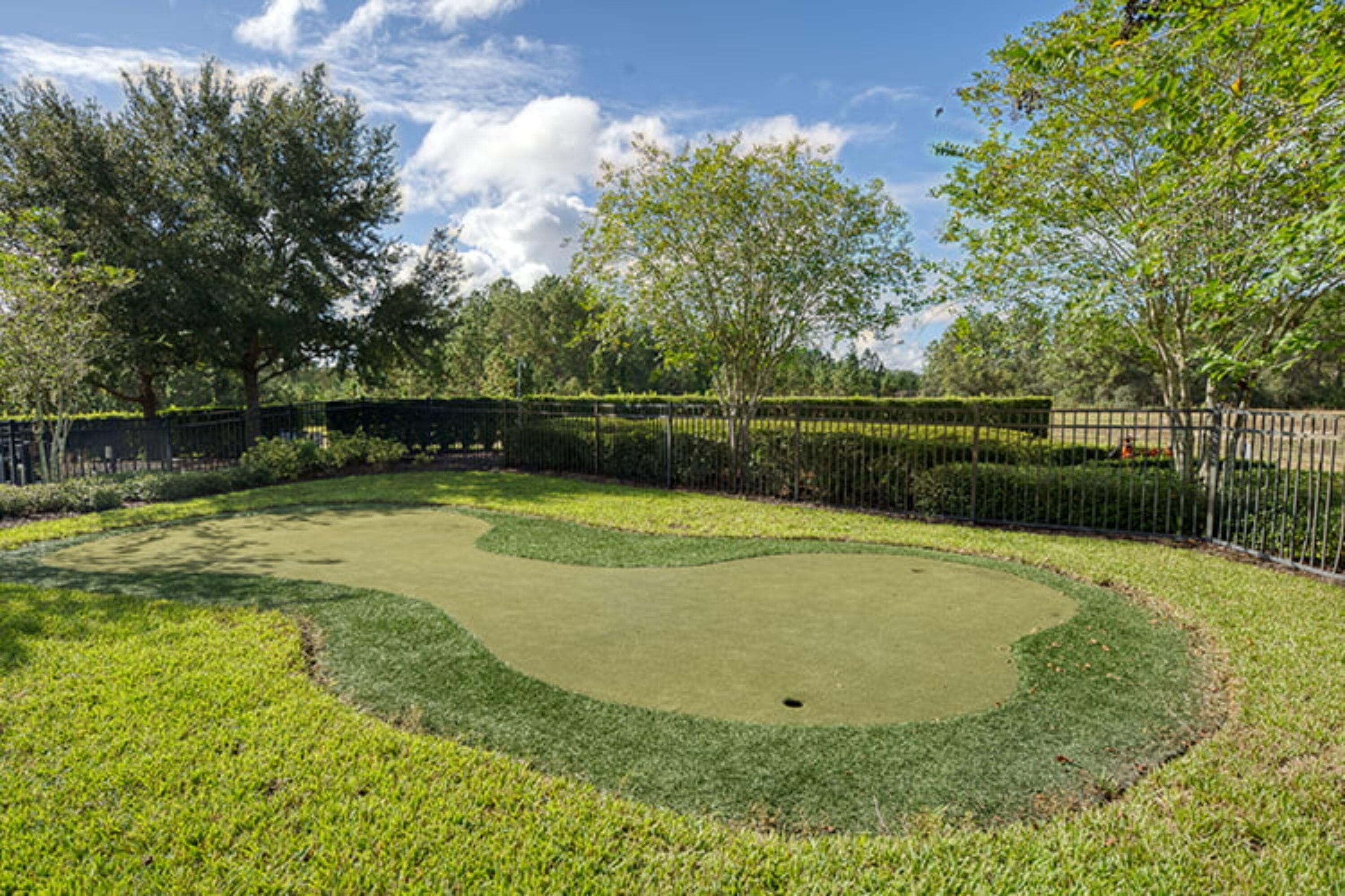 Ein gepflegter Golfplatz mit Putting-Green, umgeben von ordentlich geschnittenen Hecken und Bäumen.