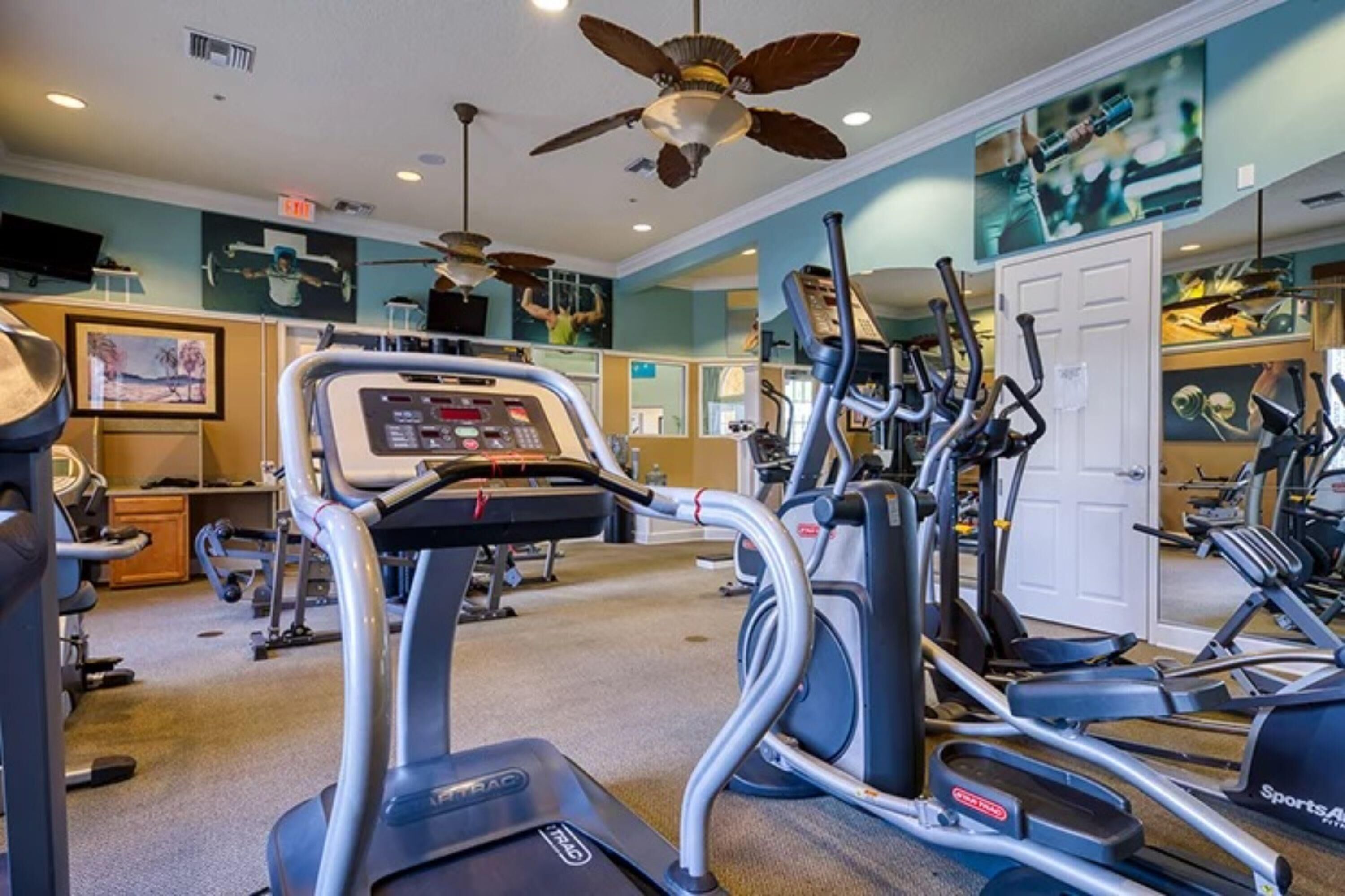 A gym with treadmills, elliptical machines, and a ceiling fan.