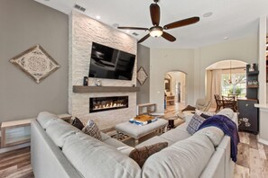 Un salon moderne doté d’une cheminée en pierre, d’un ventilateur de plafond et d’un téléviseur à écran plat fixé au mur.