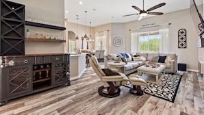 A spacious living room with a high ceiling, a ceiling fan, a sofa set, a coffee table, and a dining area with a bar. - Serenity Now by Shine Villas at Watersong #416 (Davenport)