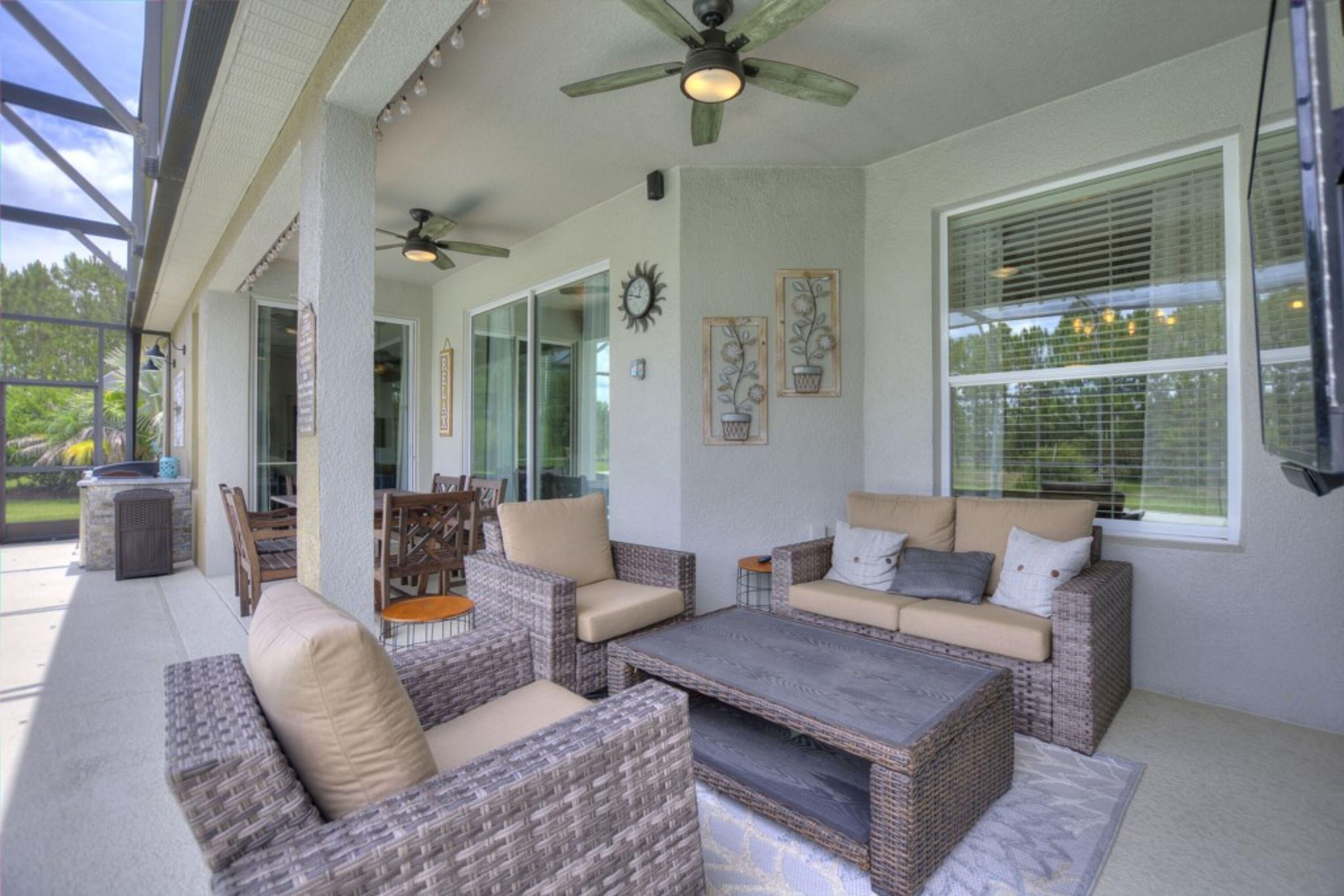 A covered patio area with wicker furniture, a ceiling fan, and a large window with blinds.