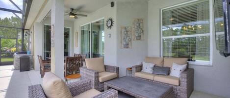 A covered patio area with wicker furniture, a ceiling fan, and a large window with blinds.