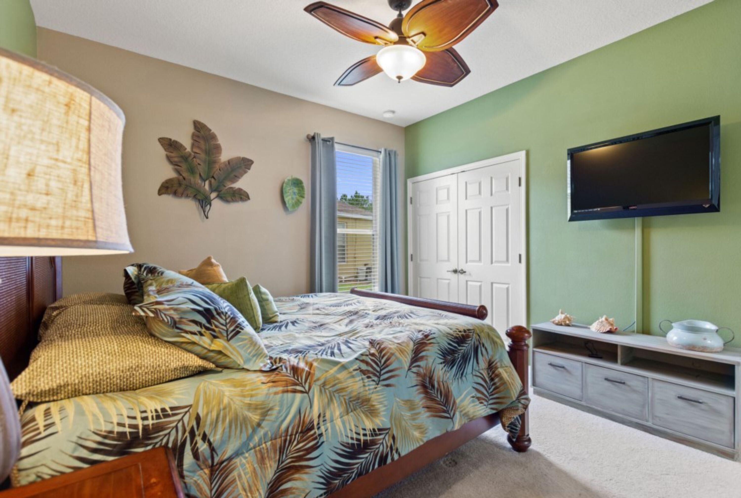 Una camera da letto con un letto, una ventola a soffitto, una TV e una porta che dà su un balcone.