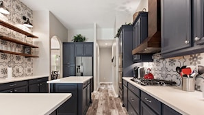 A modern kitchen with dark cabinetry, a central island, and a patterned backsplash. - Serenity Now by Shine Villas at Watersong #416 (Davenport)