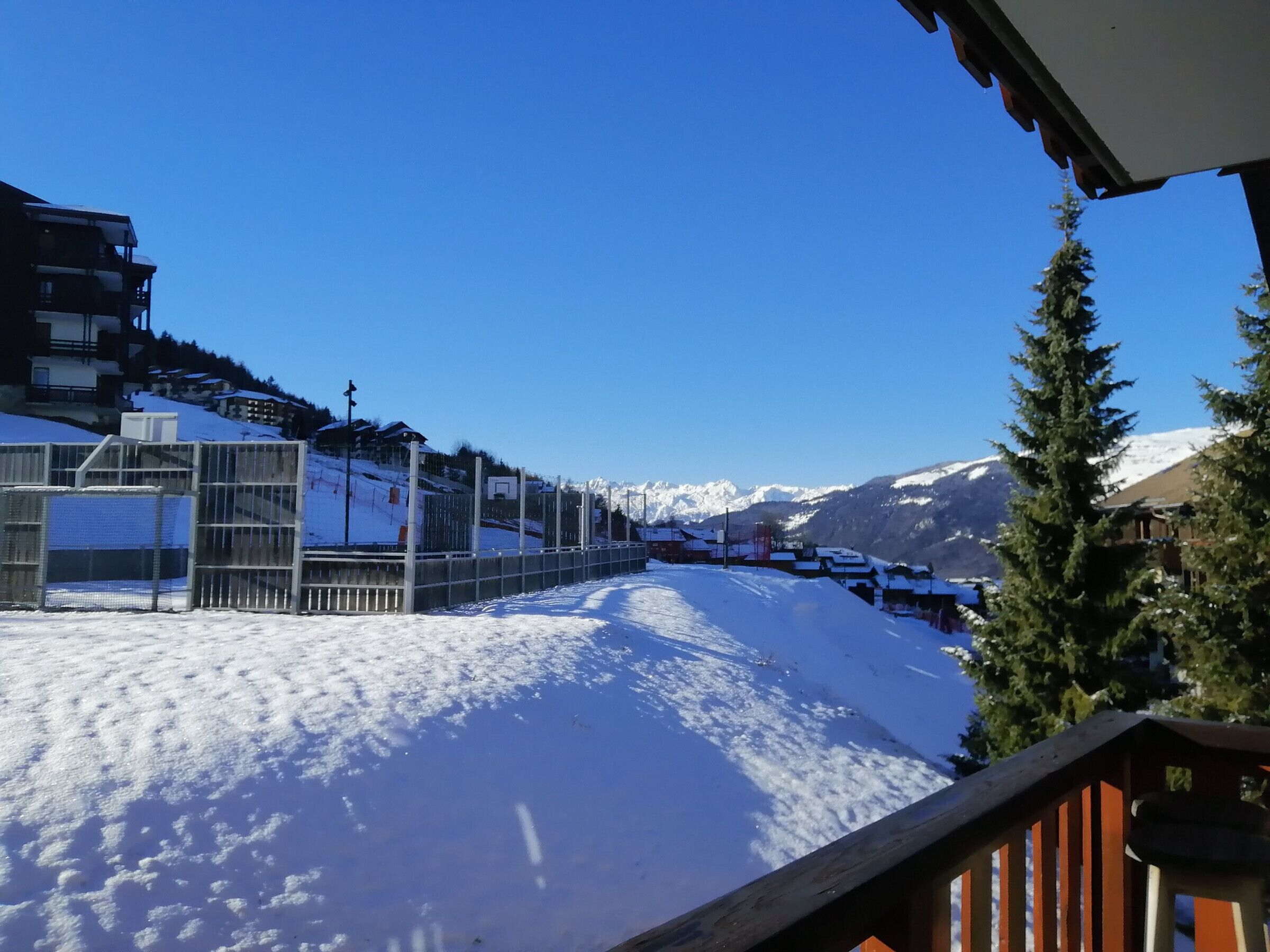 A snow-covered ski slope with buildings and a wooden fence.