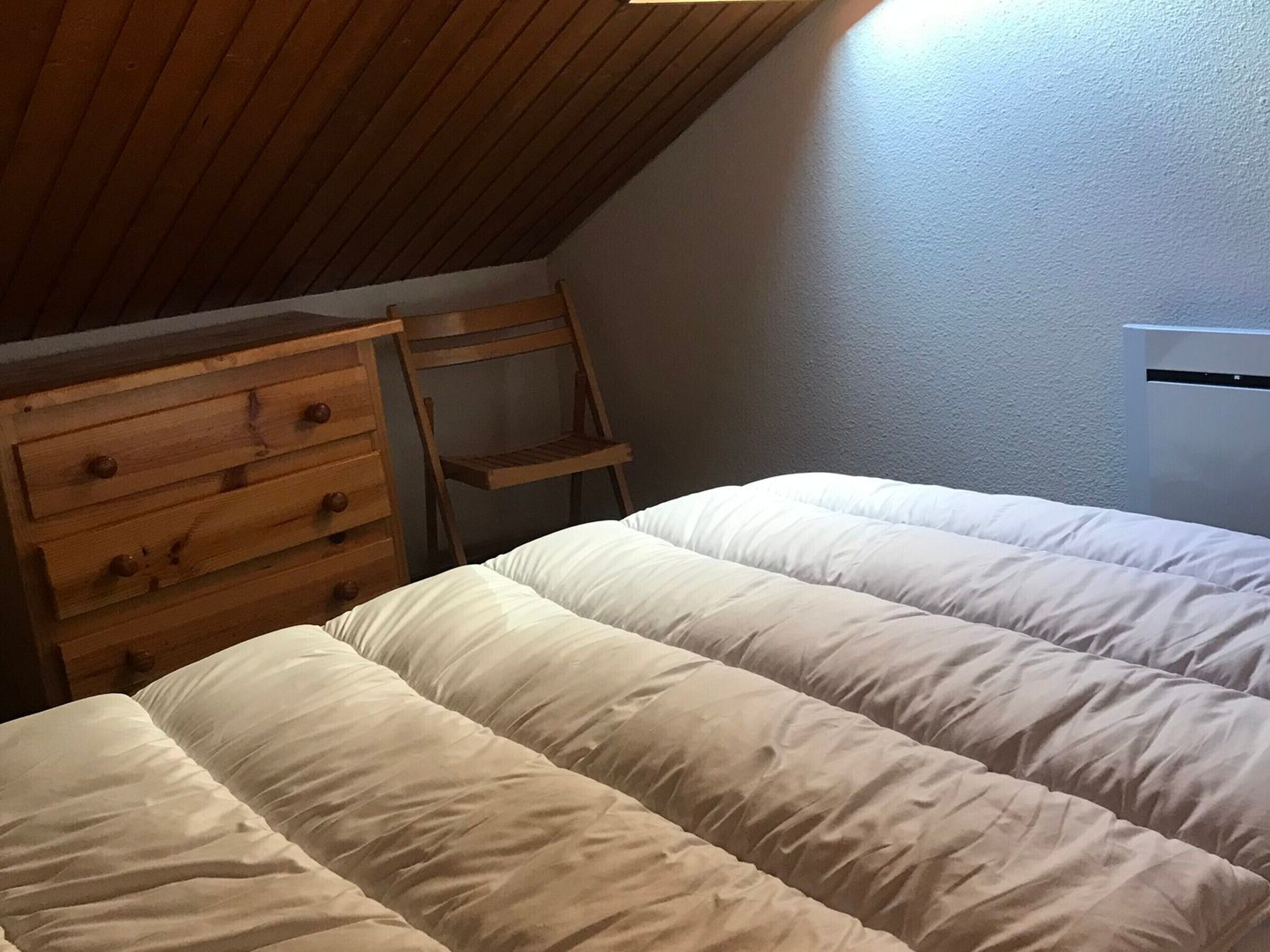 Ein Schlafzimmer mit einem Holzkasten, einem Sessel und einem Bett mit weißer Bettwäsche.