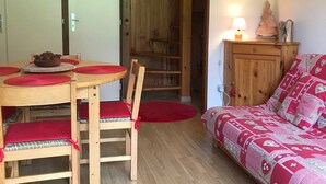 A cozy room with a wooden dining table, chairs, a red sofa, and a small cabinet with a lamp.
