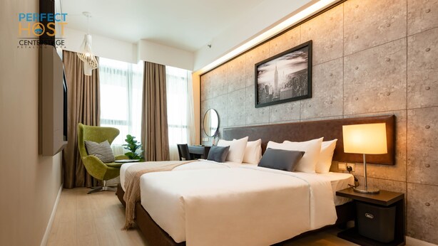 A modern hotel room with a large bed, a desk, a chair, a nightstand, and a cityscape painting on the wall. - Centrestage Petaling Jaya- Perfect Host (Petaling Jaya)