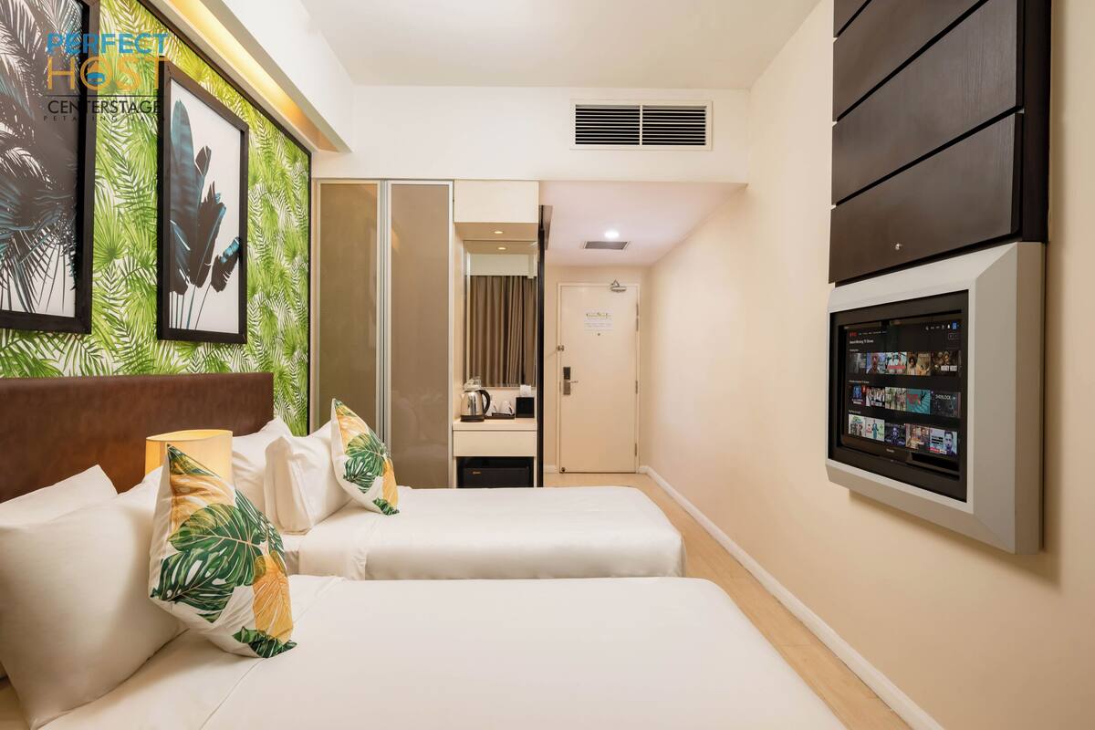 A hotel room with two beds, a TV, a minibar, and a bathroom visible through a sliding door.