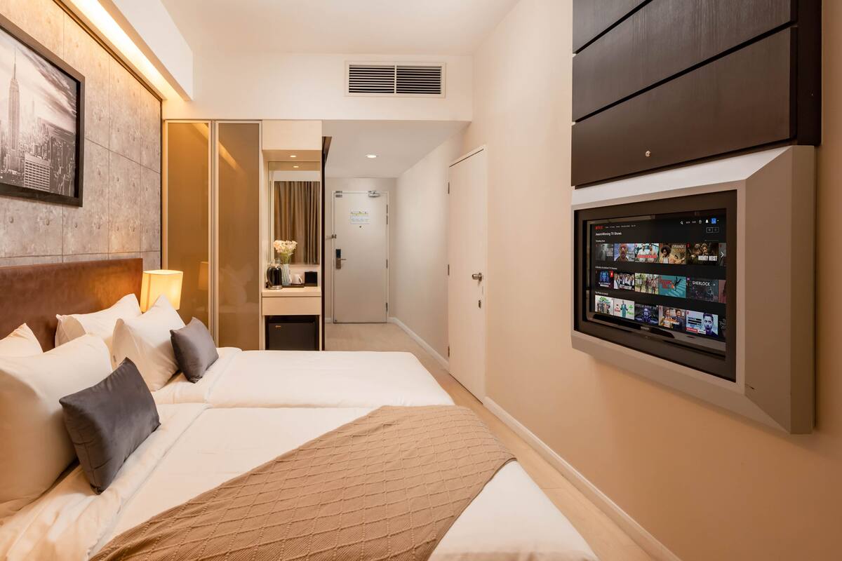 A hotel room with a bed, pillows, a TV, and a framed picture on the wall.
