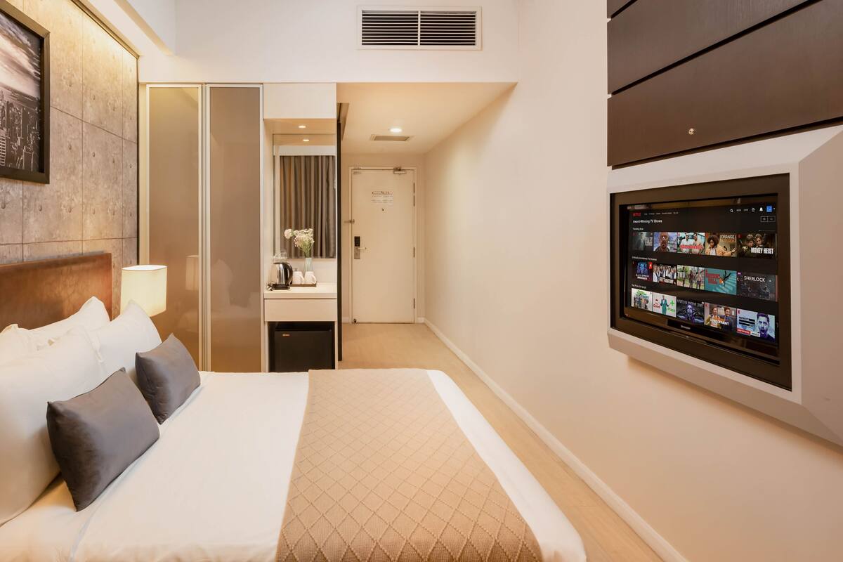 A hotel room with a large bed, a TV mounted on the wall, a cityscape painting, and a mirror.
