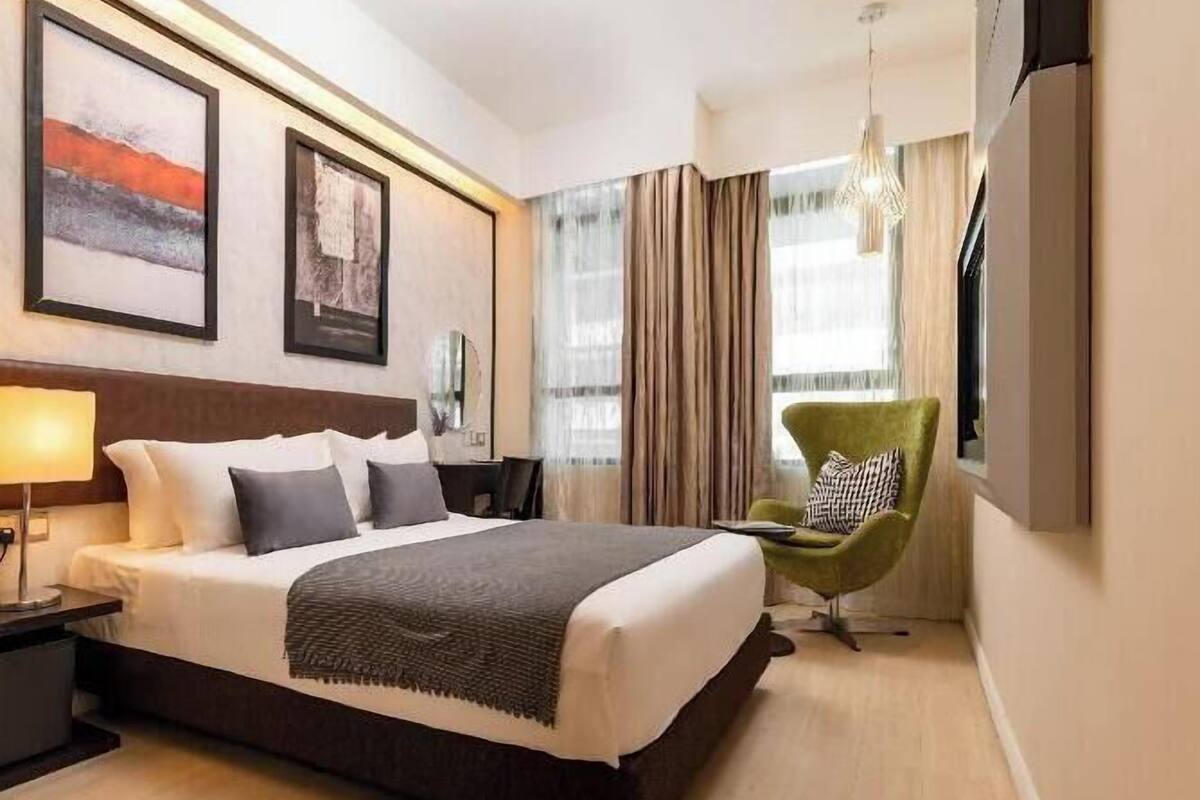 A hotel room with a bed, a desk, a chair, a TV, and artwork on the wall.
