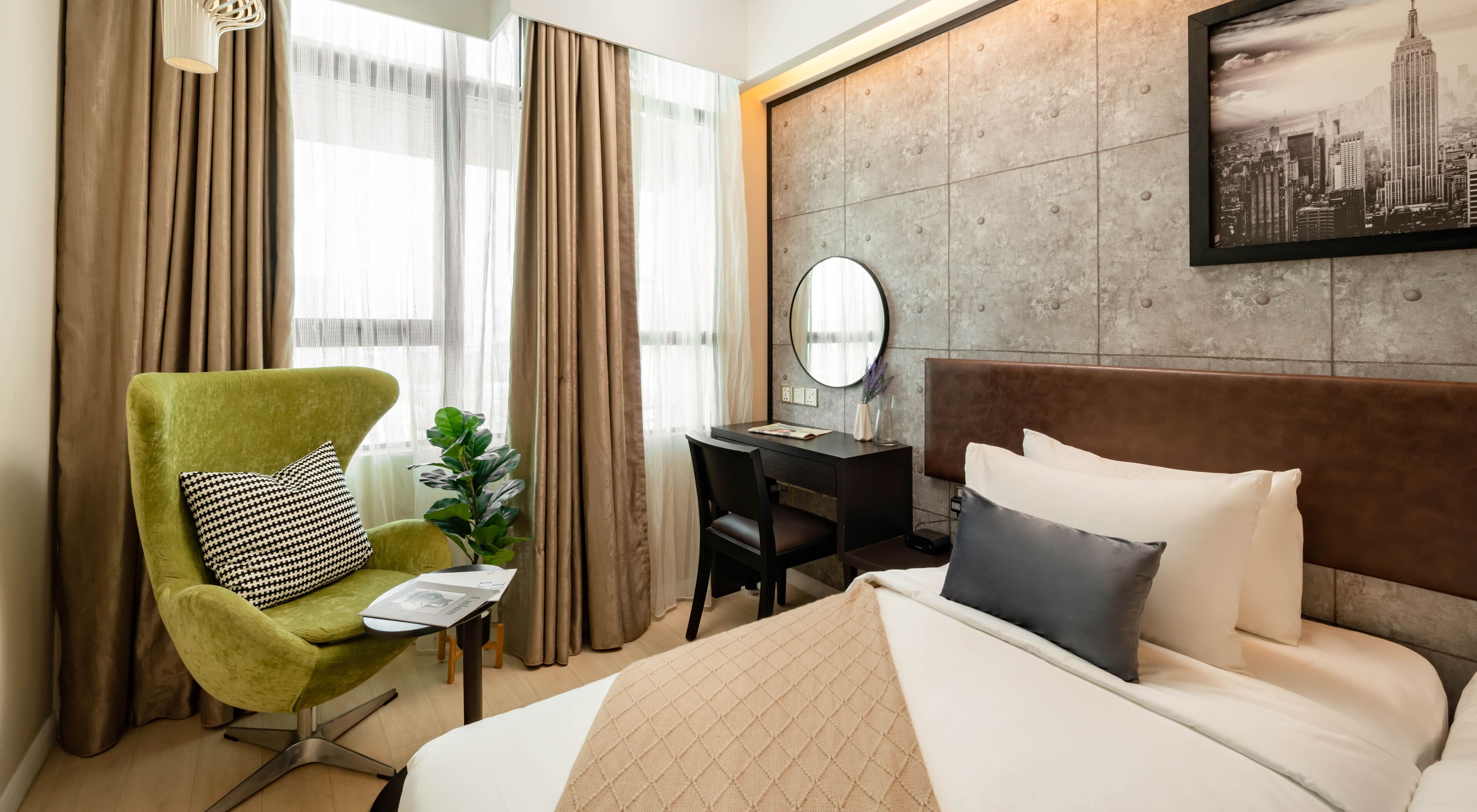 Une chambre d’hôtel avec un lit, un bureau, une chaise, un miroir et un tableau représentant un paysage urbain accroché au mur.