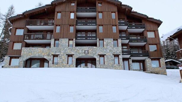 A multi-story hotel with stone and wood exterior, balconies, and a snowy landscape.