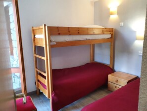 Una cama litera con escalera, una mesita de noche de madera y un colchón rojo.