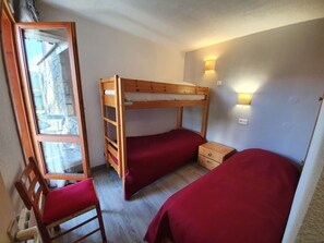 A small, cozy room with a bunk bed, a desk with a chair, and a window.