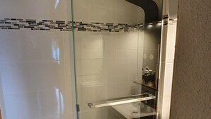 A modern bathroom with a glass shower enclosure, a white sink, and a tiled floor.