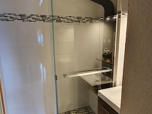 Une salle de bain moderne avec une douche à parois de verre, un lavabo blanc et un sol carrelé.