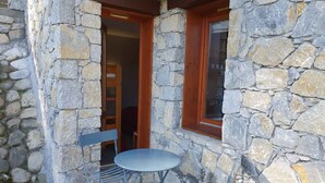 A stone building with a wooden door and window, a small round table, and a blue chair outside.