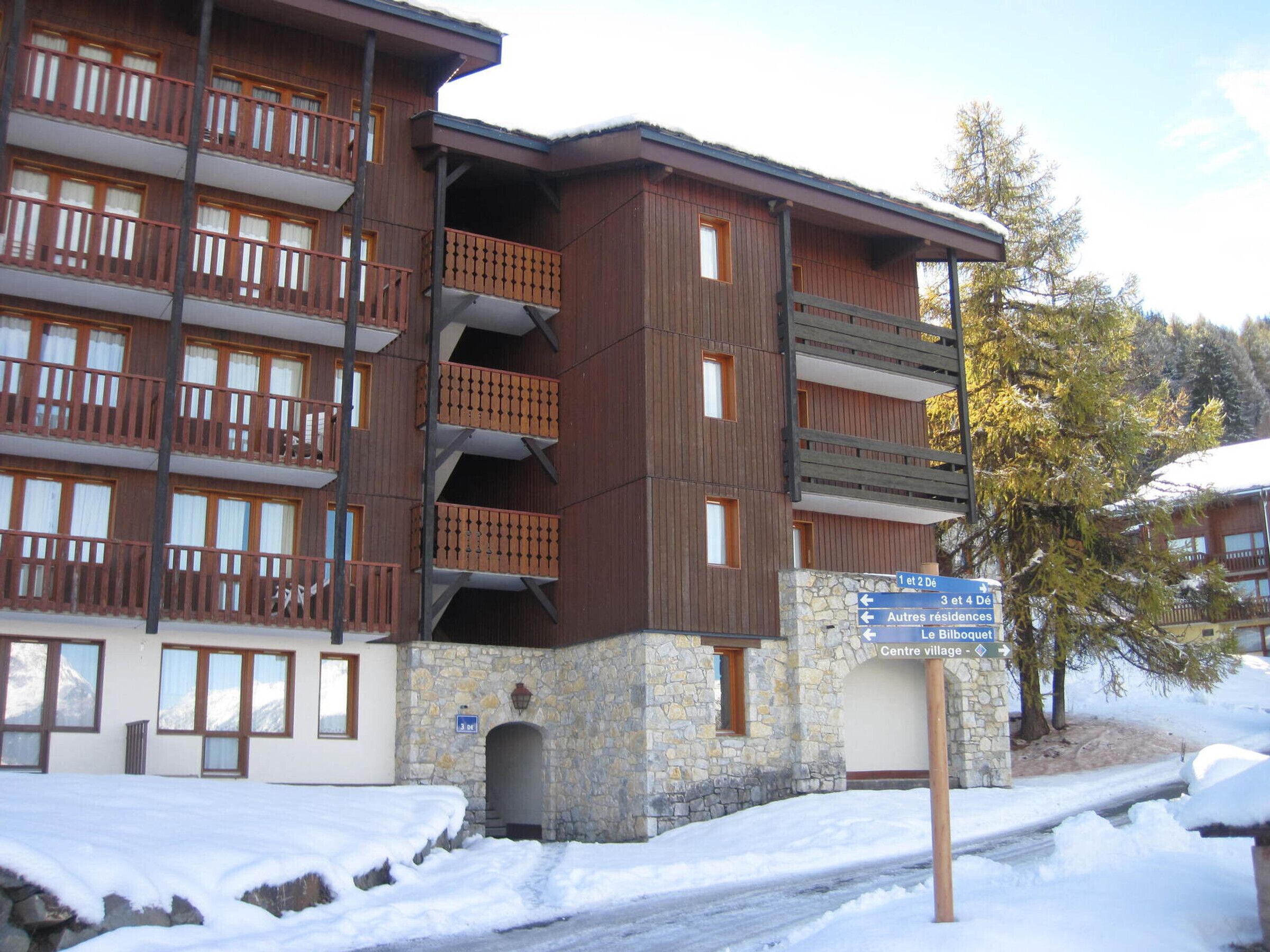 A multi-story hotel with balconies, stone facade, and a sign indicating directions to various facilities.