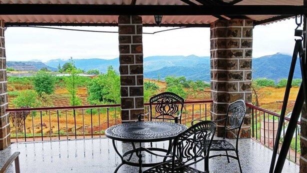 A covered outdoor area with a table and chairs, a view of a mountainous landscape, and stone pillars.