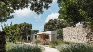A modern house with a stone wall, a paved driveway, and lush greenery. - Agroturismo Malbuger Nou - Adults only (Mahón)