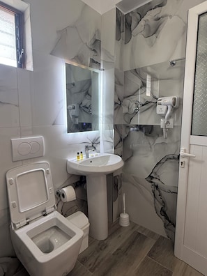 Un baño con inodoro, lavabo, espejo y una pared con diseño que imita el mármol.