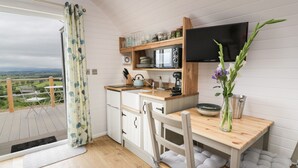 A compact kitchen with a wooden countertop, white cabinets, and a built-in TV. A dining area with a table and chairs is adjacent to the kitchen. - Laird Lodge 3 (Lochmaben)