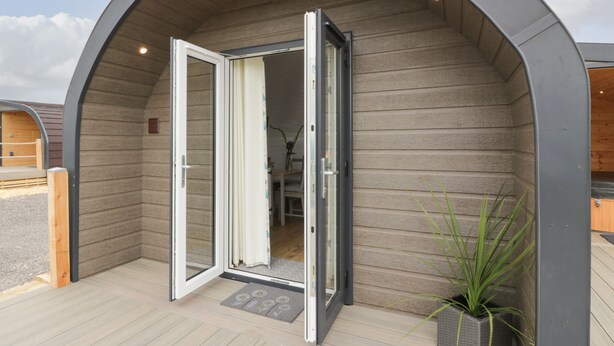A modern building with a curved entrance, a sliding glass door, and a wooden deck. - Laird Lodge 3 (Lochmaben)