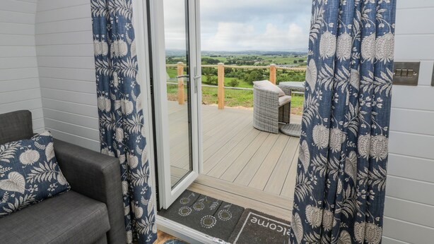 A balcony with a view of the countryside, a wicker chair, and a doormat with "Welcome" on it. - Laird Lodge 2 (Lochmaben)