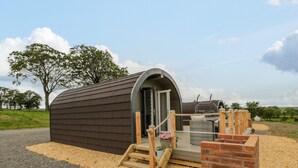 A small, single-story building with a curved roof, a wooden porch, and a brick wall. - Laird Lodge 2 (Lochmaben)