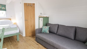 A room with a bed, a grey sofa, a wooden door, and a small table with a green cushion. - Laird Lodge 5 (Lochmaben)