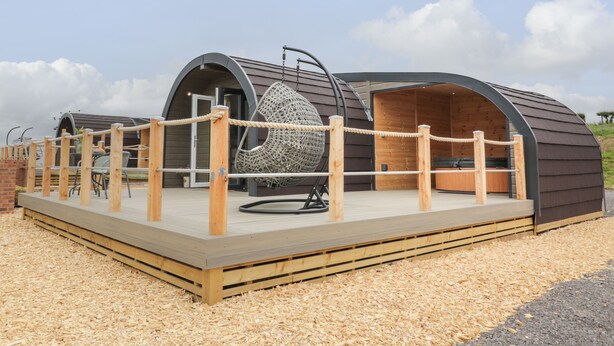 A modern building with two large arched structures, a wooden deck with a rope fence, and a hanging chair. - Laird Lodge 5 (Lochmaben)