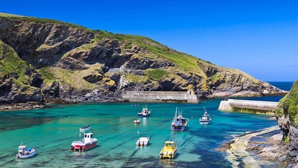Una bahía costera con barcos anclados cerca de un rompeolas rocoso.