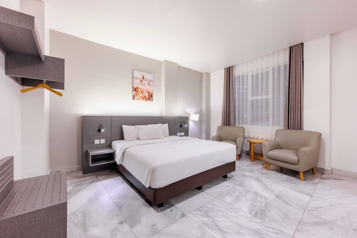 A modern hotel room with a large bed, a bedside table, a chair, and a small table.