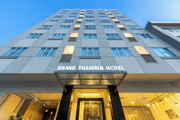 La façade de l’hôtel Grand Thamrin présente un design moderne, avec de nombreuses fenêtres et une entrée imposante.