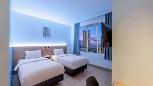 A hotel room with two beds, a desk, and a view of the cityscape. - GRAND   THAMRIN  HOTEL (Jakarta)
