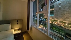 A hotel room with a bed, bedside phone, and a window with a view of a cityscape at night. - GRAND   THAMRIN  HOTEL (Jakarta)