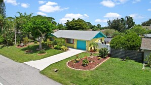 Una casa a un piano con un portone del garage blu, immersa in un prato curato e circondata da varie piante.