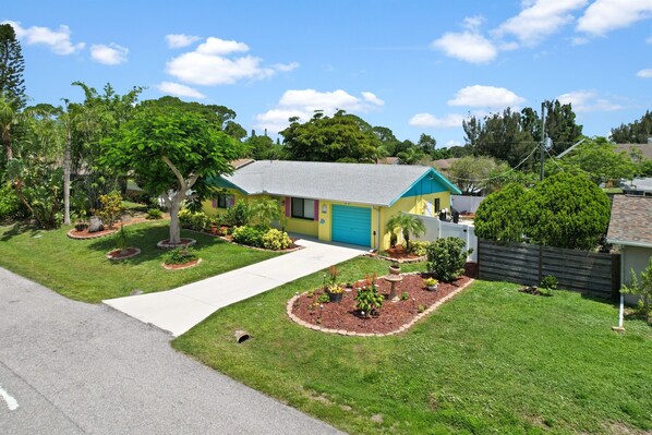 A single-story house with a blue garage door, surrounded by a well-maintained lawn and various plants. - Creative Coastal Cottage - 5 min to beach (Venice)