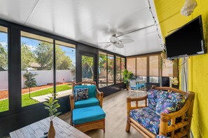 A covered patio with wicker furniture, a ceiling fan, and a TV mounted on the wall. - Creative Coastal Cottage - 5 min to beach (Venice)