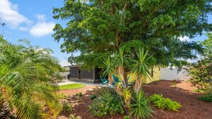 Un giardino curato con diverse piante, una zona patio con sedie e un edificio dal design moderno.