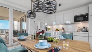 A modern kitchen with Bosch appliances, a dining area with a wooden table set for a meal, and a view of the city through large windows. - Sloop-Lounge - Fireplace, Infrared Sauna, Bathtub, Shower, Balcony, 2 Floors (Olpenitz)