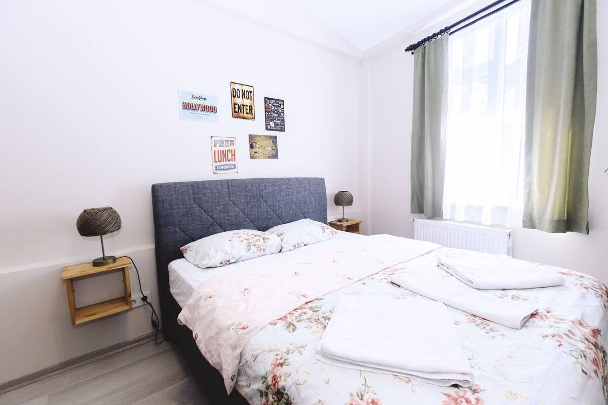 A neatly made bed with floral bedding, a grey headboard, and a bedside table with a lamp.