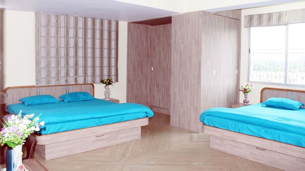 Una habitación con dos camas, cada una con cubrecama azul, cabeceros de madera y una mesita de noche con un jarrón de flores.