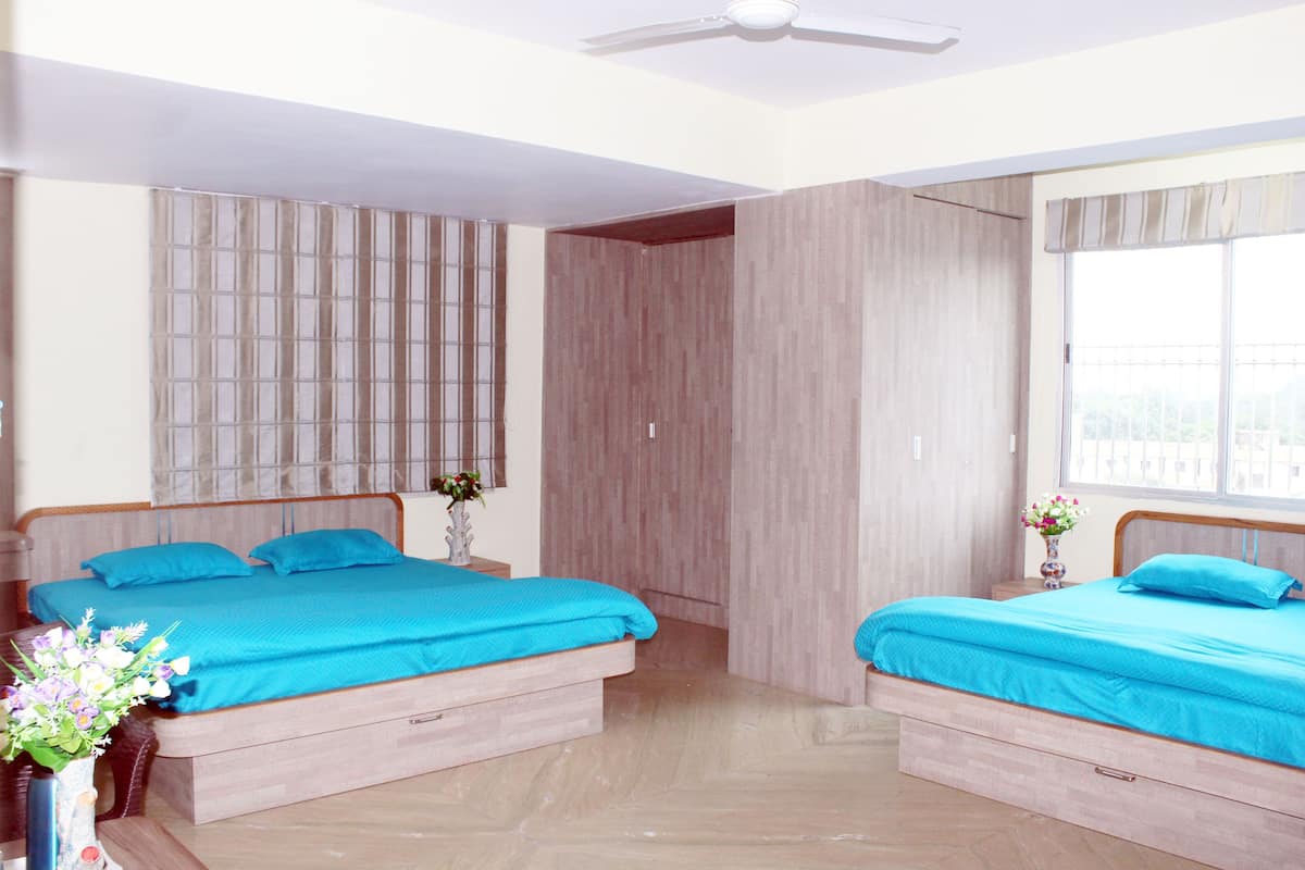 Una habitación con dos camas, cada una con cubrecama azul, cabeceros de madera y una mesita de noche con un jarrón de flores.