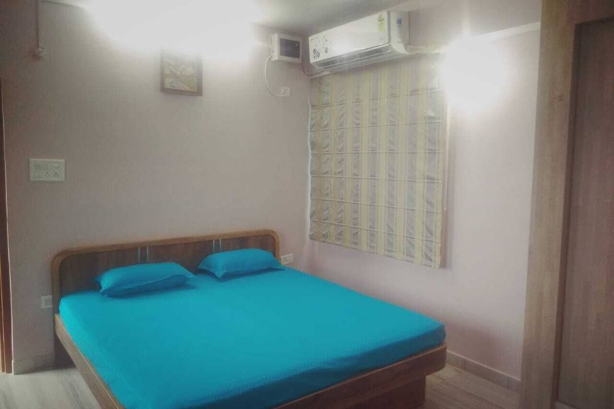 Un dormitorio con cama, ventana con persianas, equipo de aire acondicionado y una puerta.